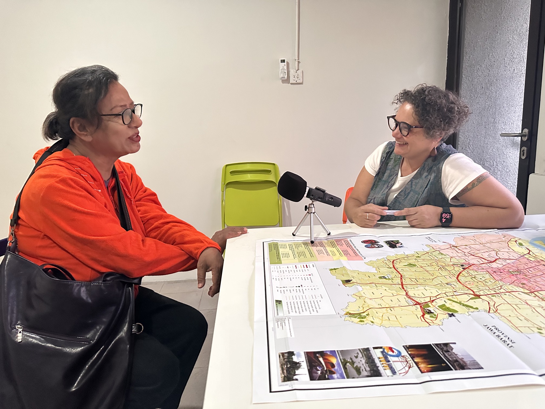 Two practitioners in conversation over a regional map with a recording microphone